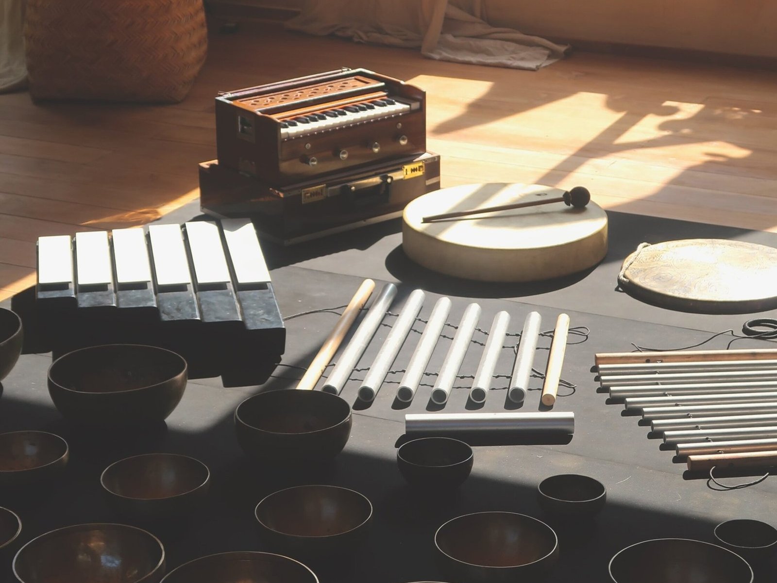 A variety of professional sound healing instruments including a harmonium, frame drum, chimes, and brass singing bowls arranged on a floor studio