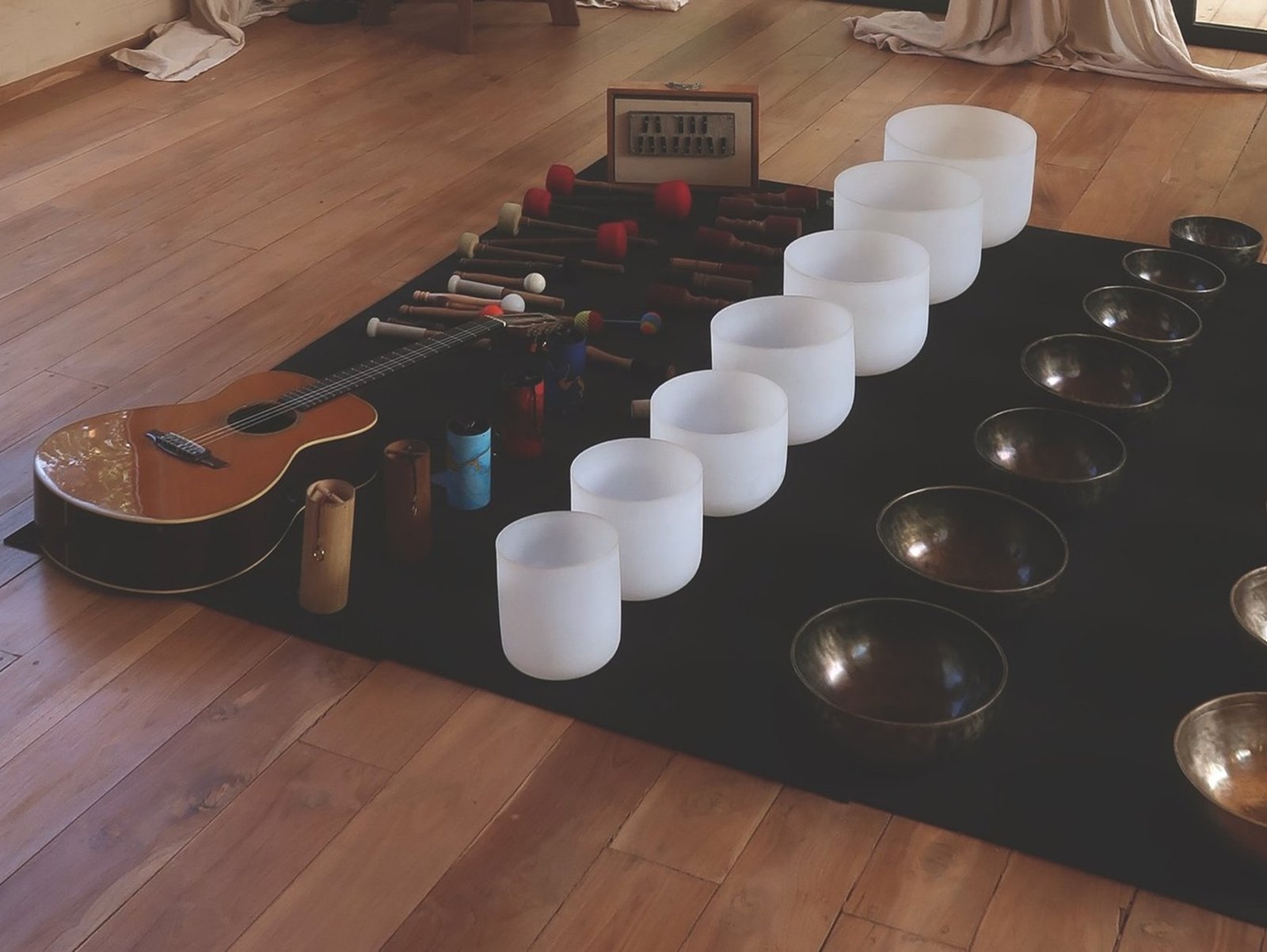 A clean alignment of white frosted crystal singing bowls next to an acoustic guitar and therapeutic mallets