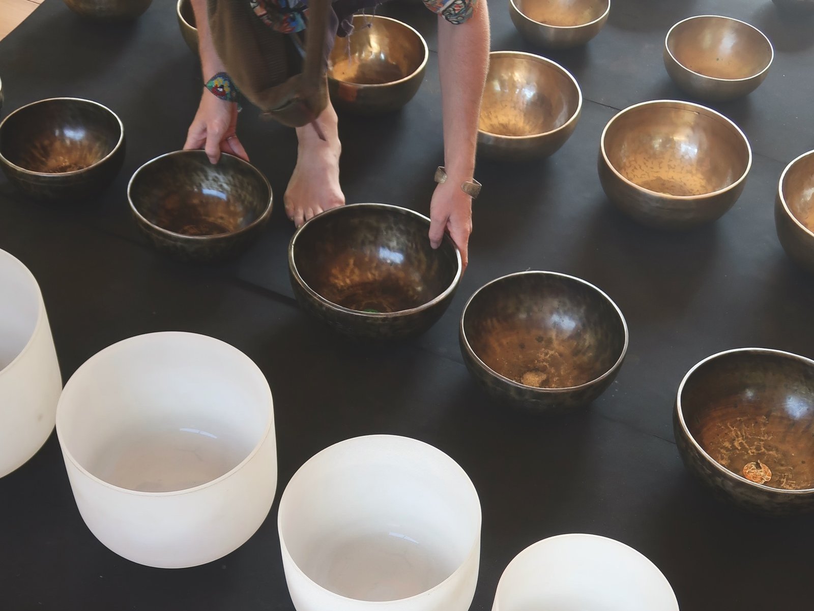 Male sound healing practitioner playing a brass singing bowl surrounded by a large collection of Tibetan bowls in Sri Lanka